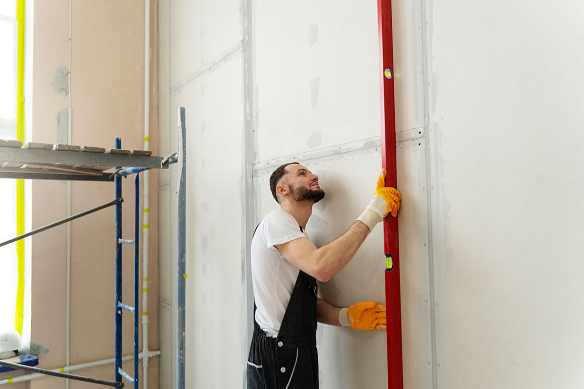 Man putting up drywall with a tool.
